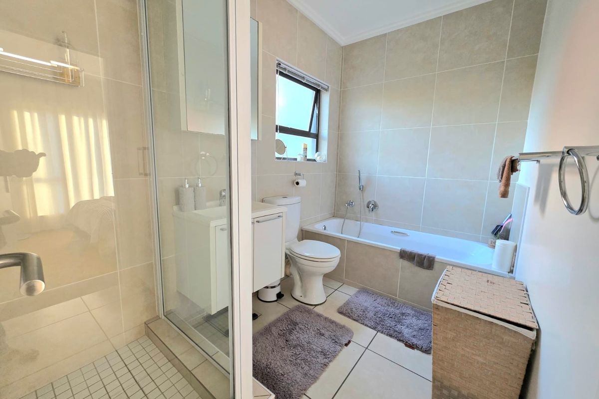 A well-maintained bathroom featuring a separate shower enclosure, bathtub, vanity cabinet, and neutral floor-to-ceiling wall tiling.