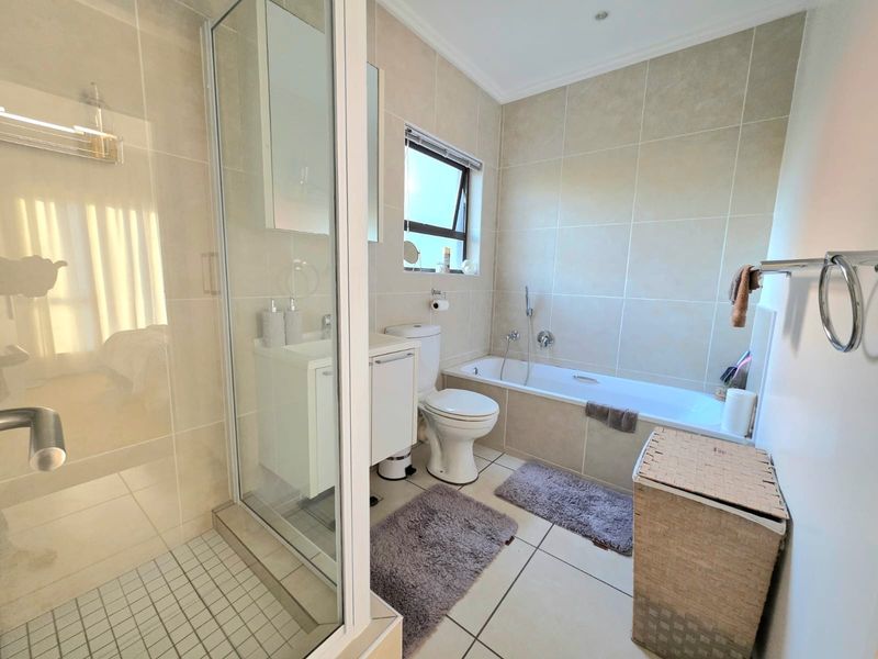 A well-maintained bathroom featuring a separate shower enclosure, bathtub, vanity cabinet, and neutral floor-to-ceiling wall tiling.
