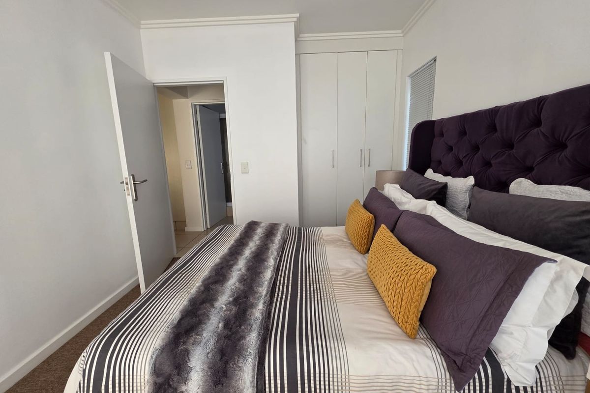 A well-maintained bedroom featuring neutral walls, carpeted flooring, and built-in cupboards with direct access to an adjoining room.