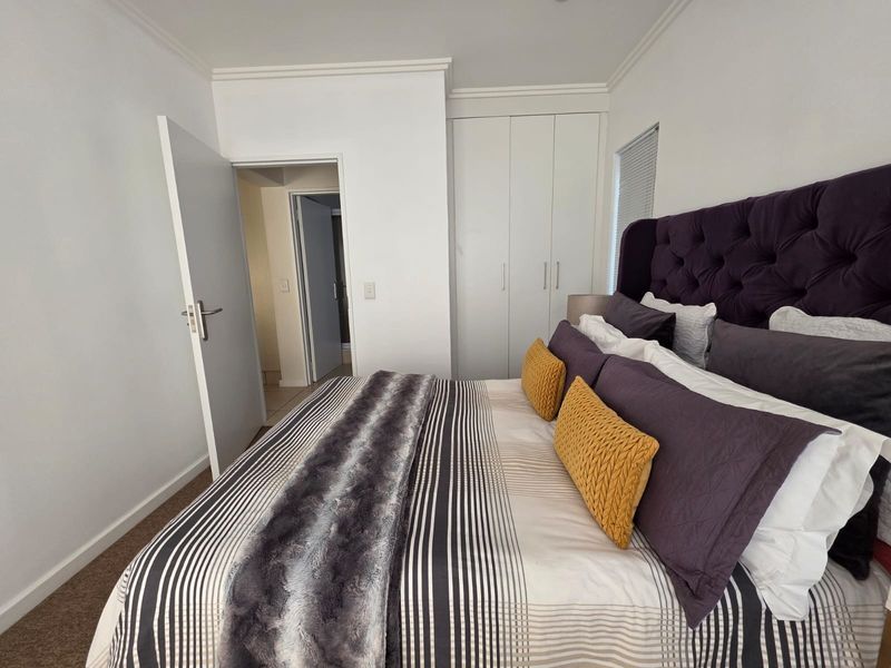 A well-maintained bedroom featuring neutral walls, carpeted flooring, and built-in cupboards with direct access to an adjoining room.