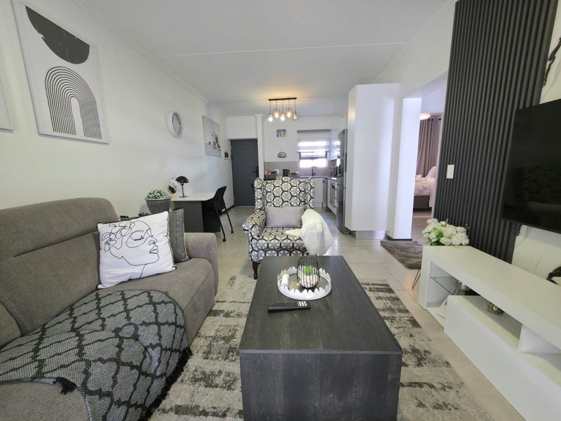An open-plan living area featuring tiled floors, a modern slatted feature wall, and a seamless transition into the kitchen and adjacent bedroom space.