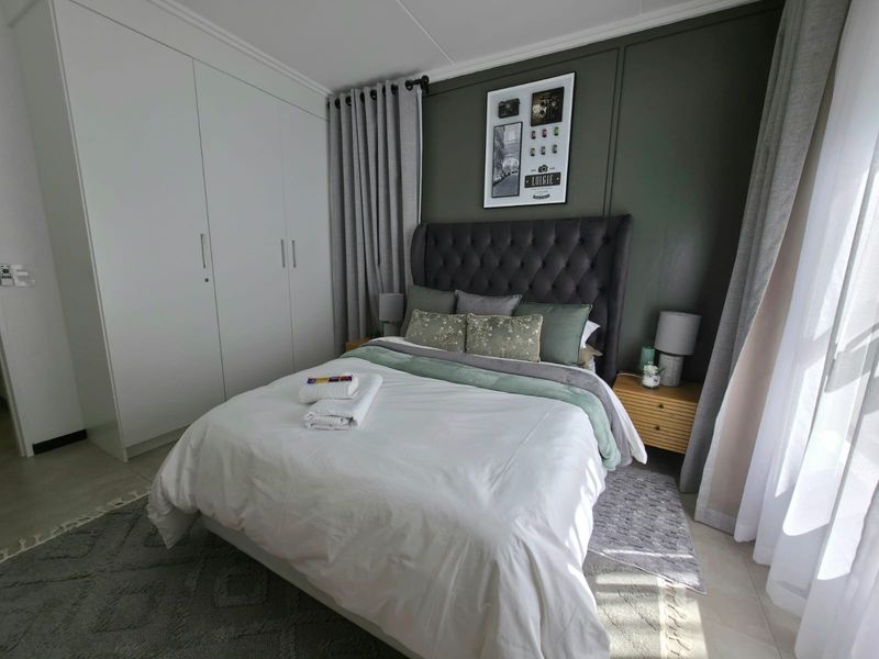 A well-maintained bedroom featuring built-in cupboards, tiled flooring, and a feature wall with neutral finishes.