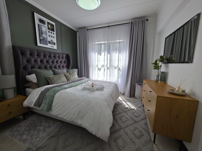 A well-maintained bedroom featuring an olive green accent wall, neutral flooring, and large windows with floor-to-ceiling curtains.