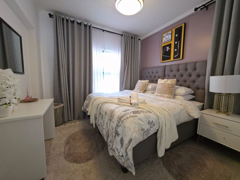 A well-maintained bedroom featuring neutral tones, a feature wall, and large windows with floor-to-ceiling curtains.