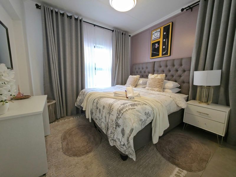 A well-maintained bedroom featuring neutral tones, tiled flooring, and large windows with floor-to-ceiling curtains, creating a bright and comfortable living space.