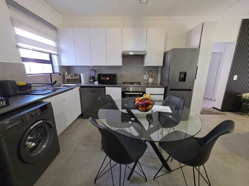 Modern kitchen featuring white cabinetry, stainless steel appliances, gas hob, extractor fan, and tiled flooring, integrated with a dining area.