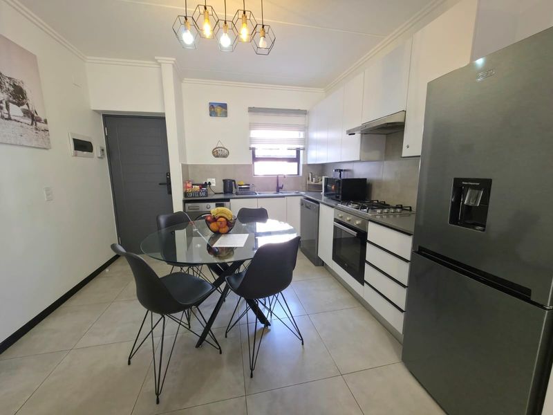 Modern open-plan kitchen featuring sleek white cabinetry, gas hob, integrated oven, and tiled flooring, seamlessly flowing into a functional dining area.