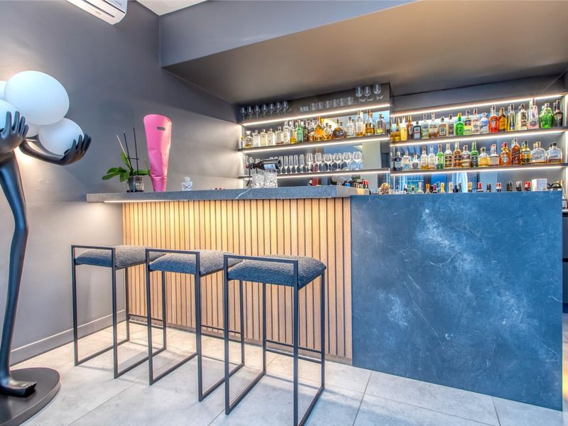 A modern, well-appointed home bar featuring a slatted timber and stone-look counter, integrated LED-lit shelving, and contemporary tiled flooring.