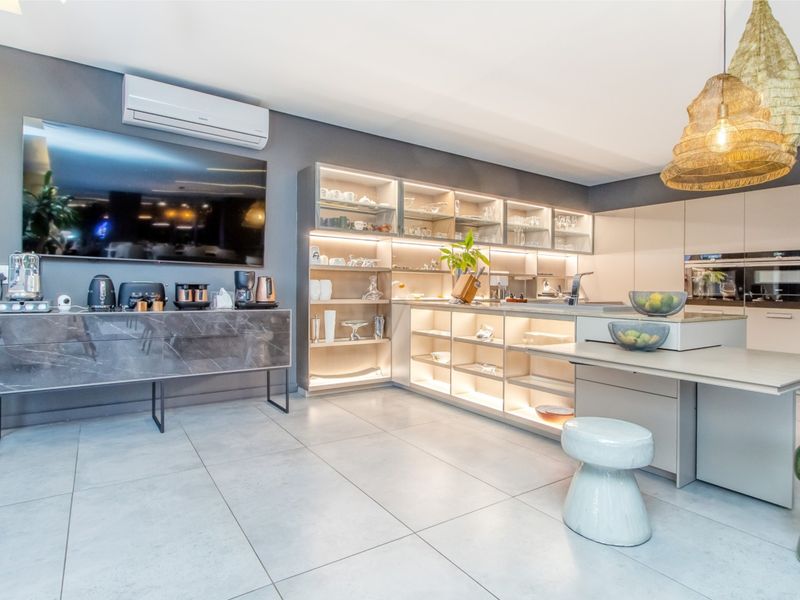 Modern, high-end kitchen featuring sleek built-in cabinetry, integrated display shelving with ambient lighting, large format floor tiles, and premium built-in appliances.