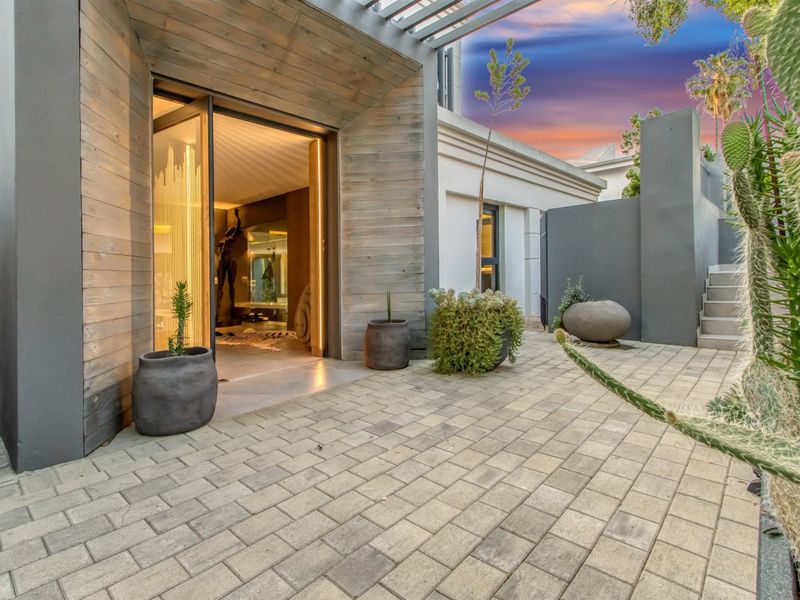 A modern paved patio area featuring timber-clad walls, a pergola structure, and concrete stairs leading to an elevated section of the property.