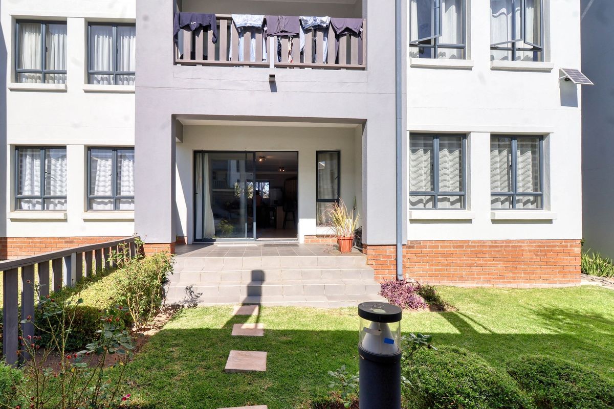 Rear view of the apartment building featuring a ground floor patio with sliding door access, a balcony above, and a small private garden area.