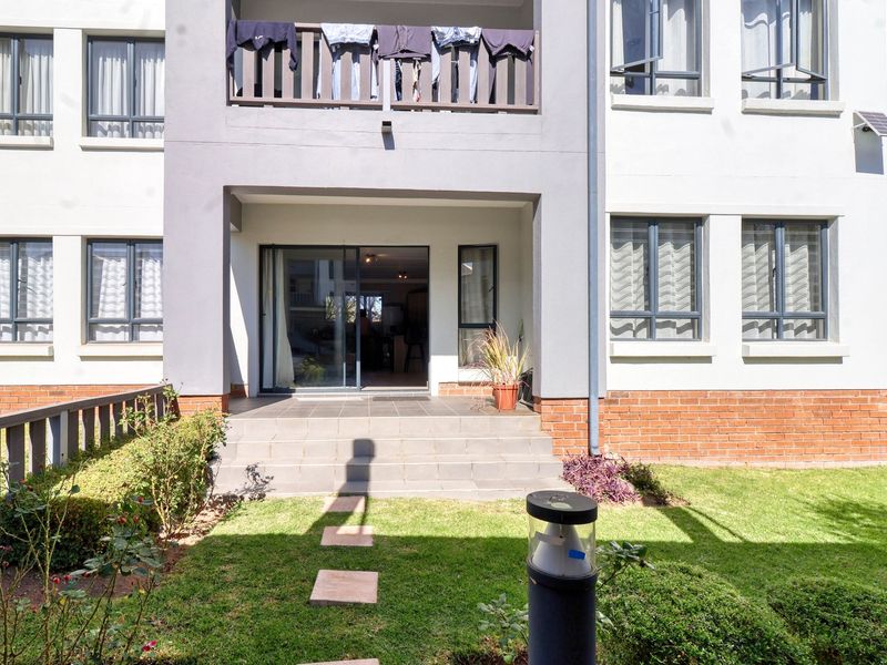 Rear view of the apartment building featuring a ground floor patio with sliding door access, a balcony above, and a small private garden area.