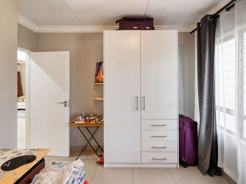 A bedroom featuring a white built-in wardrobe, tiled flooring, and neutral wall finishes, providing a functional and clean living space.