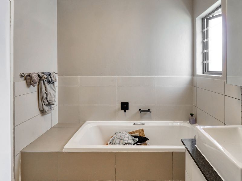 A modern bathroom featuring a built-in bathtub with wall-mounted fixtures, tiled surround, and a vanity basin with a granite countertop.