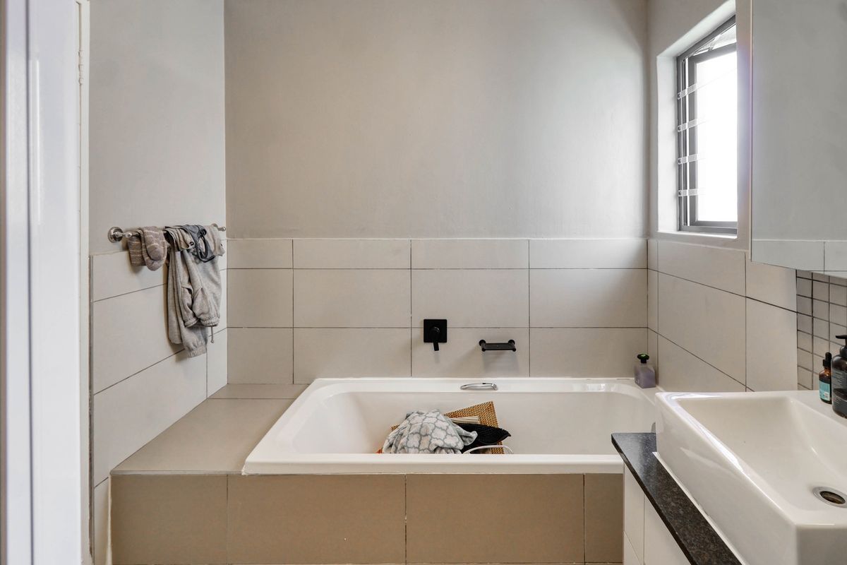 A modern bathroom featuring a built-in bathtub with wall-mounted fixtures, tiled surround, and a vanity basin with a granite countertop.