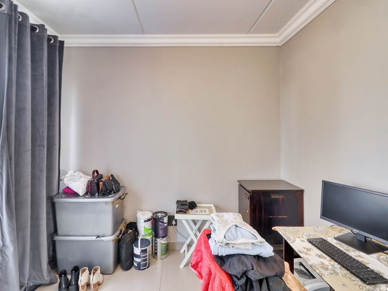 A bedroom space featuring neutral wall tones, crown molding, and tiled flooring, offering a versatile area for a home office or sleeping quarters.