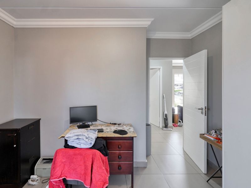 A functional office space featuring neutral wall tones, crown molding, and tiled flooring, with a doorway leading to an adjacent area.