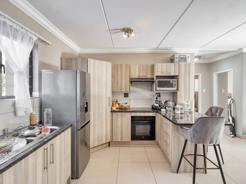 A functional kitchen featuring light wood cabinetry, granite countertops, built-in oven, hob, extractor fan, and tiled flooring with a breakfast nook.