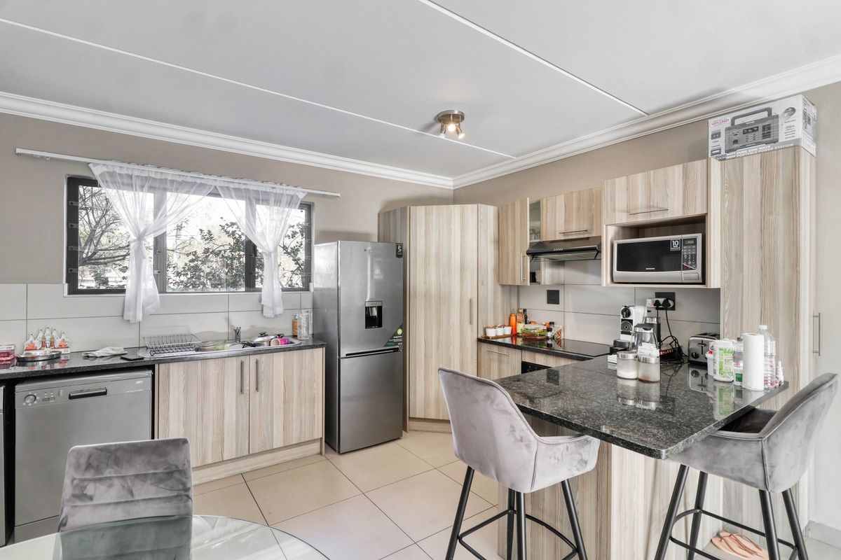 A functional kitchen featuring light wood-finish cabinetry, granite countertops, integrated microwave, extractor fan, and tiled flooring with a breakfast bar area.
