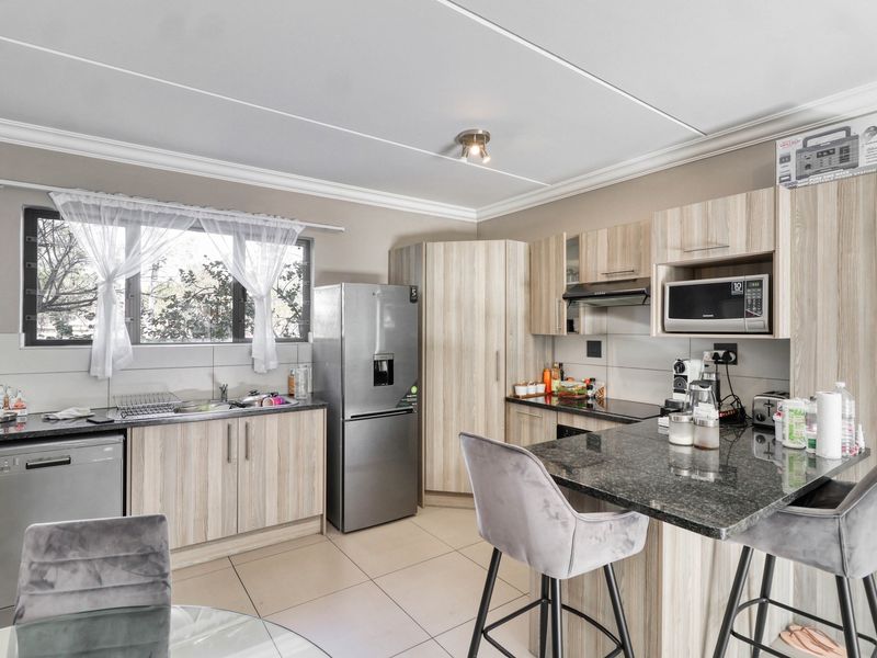 A functional kitchen featuring light wood-finish cabinetry, granite countertops, integrated microwave, extractor fan, and tiled flooring with a breakfast bar area.