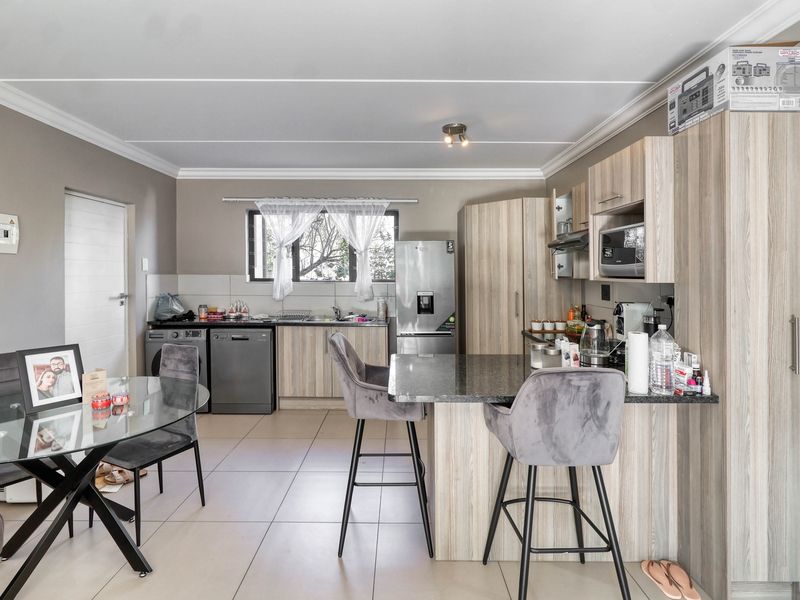 Open-plan kitchen and dining area featuring modern wood-finish cabinetry, granite countertops, a functional kitchen island, and neutral tiled flooring throughout.