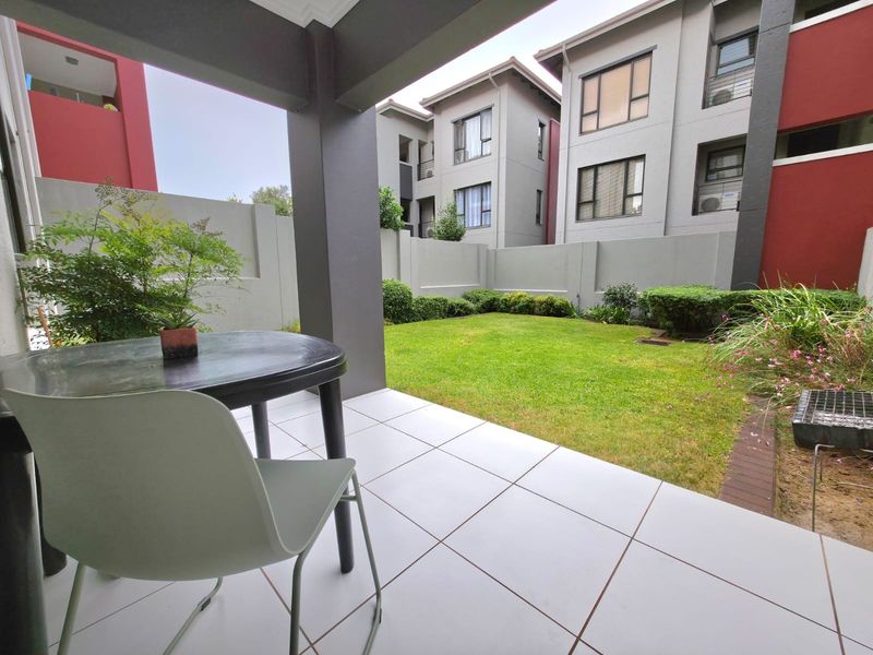 A covered patio area with tiled flooring overlooking a private garden and surrounding apartment complex buildings.