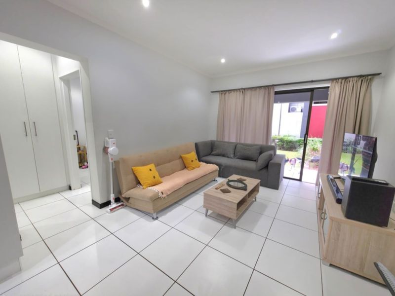 A bright living room featuring white tiled flooring, built-in storage cupboards, and a sliding glass door providing access to the outdoor area.