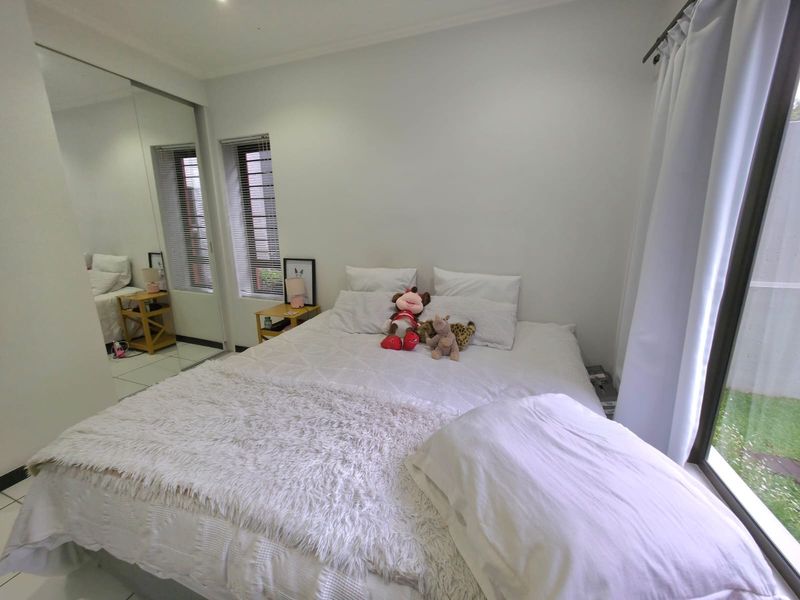 A bright bedroom featuring tiled flooring, mirrored sliding wardrobe doors, and a large sliding glass door providing access to the exterior.