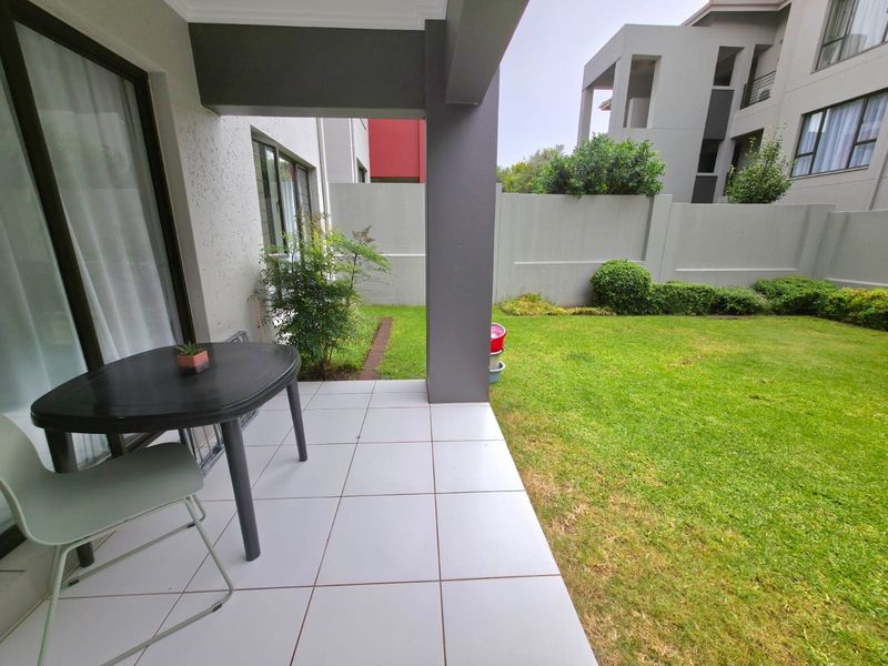 A covered patio with tiled flooring, providing direct access to a private garden area and enclosed by a boundary wall.