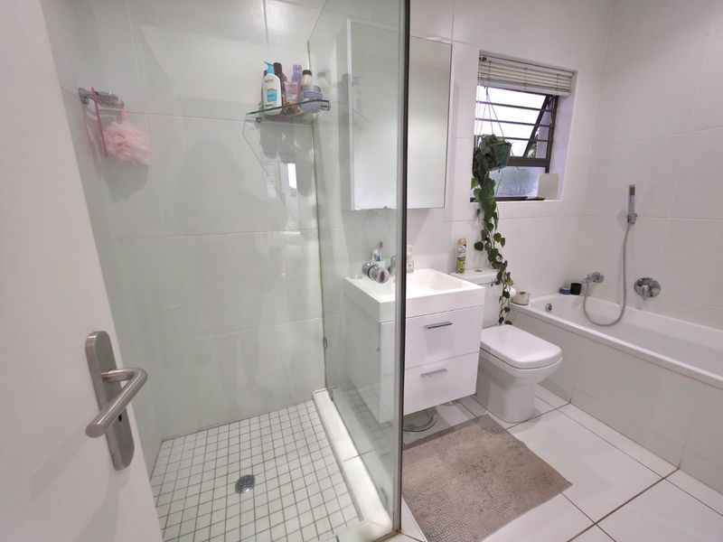Modern bathroom featuring a glass-enclosed shower, a separate bathtub, a vanity unit with basin, and a toilet, finished with clean white wall and floor tiles.