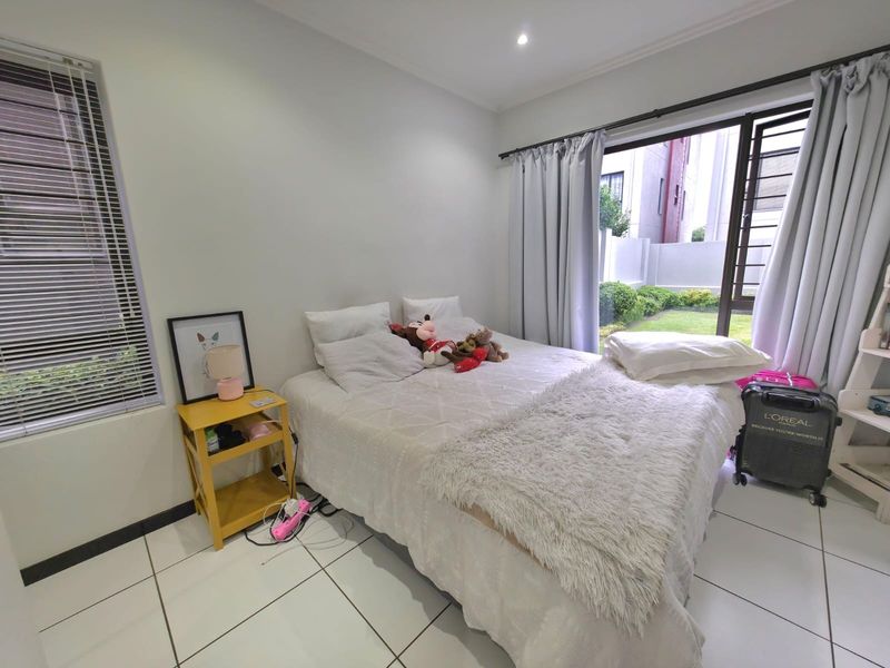 A bright bedroom featuring white tiled flooring, recessed lighting, and a sliding glass door providing direct access to the garden area.