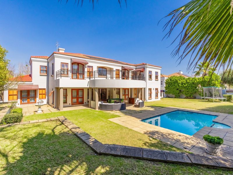 Spacious rear exterior featuring a large swimming pool, covered patio, upper balcony, and well-maintained garden area.