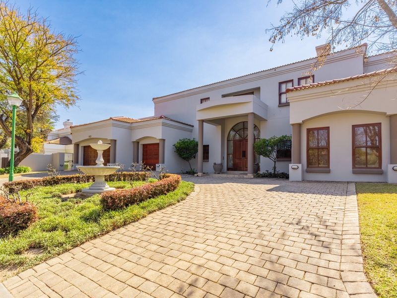 A well-maintained front exterior featuring a paved driveway, a central stone fountain, a covered entrance portico, and a double garage.