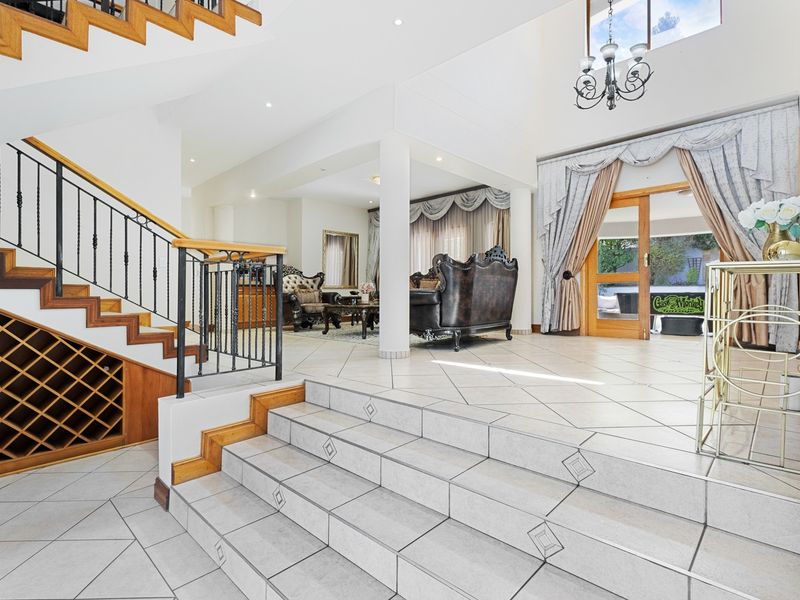 Spacious grand entrance hall featuring a tiled staircase with built-in wine storage, wrought iron railings, and direct access to the living area and patio.