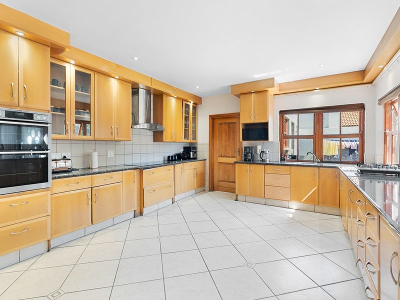 Spacious kitchen featuring extensive wooden cabinetry, granite countertops, built-in double oven, stainless steel extractor fan, and tiled flooring.