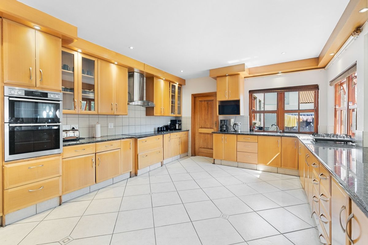 Spacious kitchen featuring extensive wooden cabinetry, granite countertops, built-in double oven, stainless steel extractor fan, and tiled flooring.