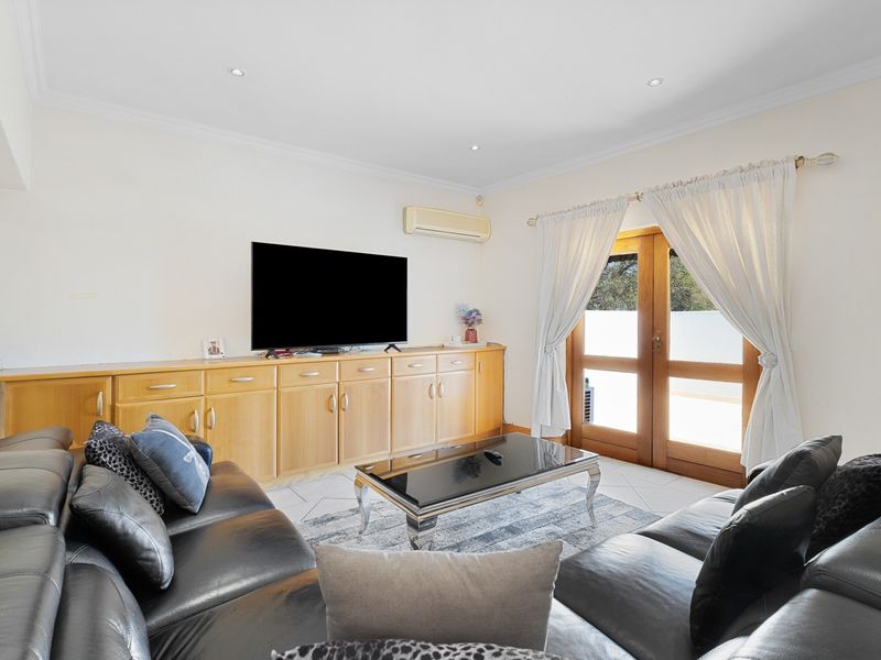 A living room featuring built-in timber cabinetry, tiled flooring, recessed lighting, and timber-framed glass doors providing access to the outdoor area.