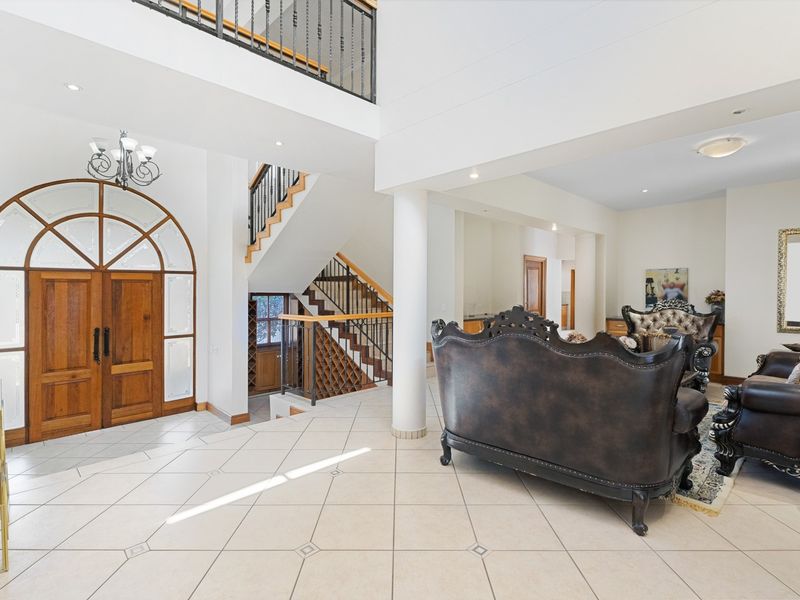 Spacious grand entrance hall featuring an arched timber door, tiled flooring, and an elegant staircase with wrought iron balustrades and integrated wine storage.