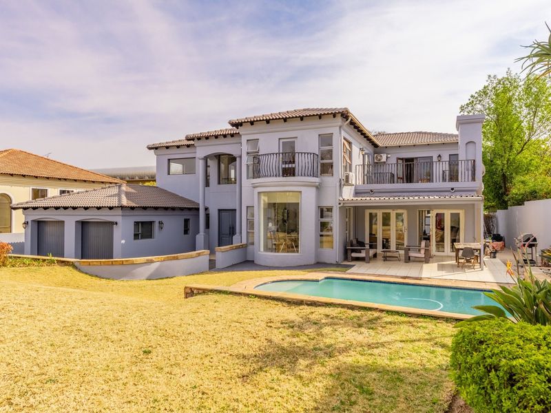 Rear view of a double-story residence featuring a swimming pool, paved patio, upper-level balcony, and attached double garage.