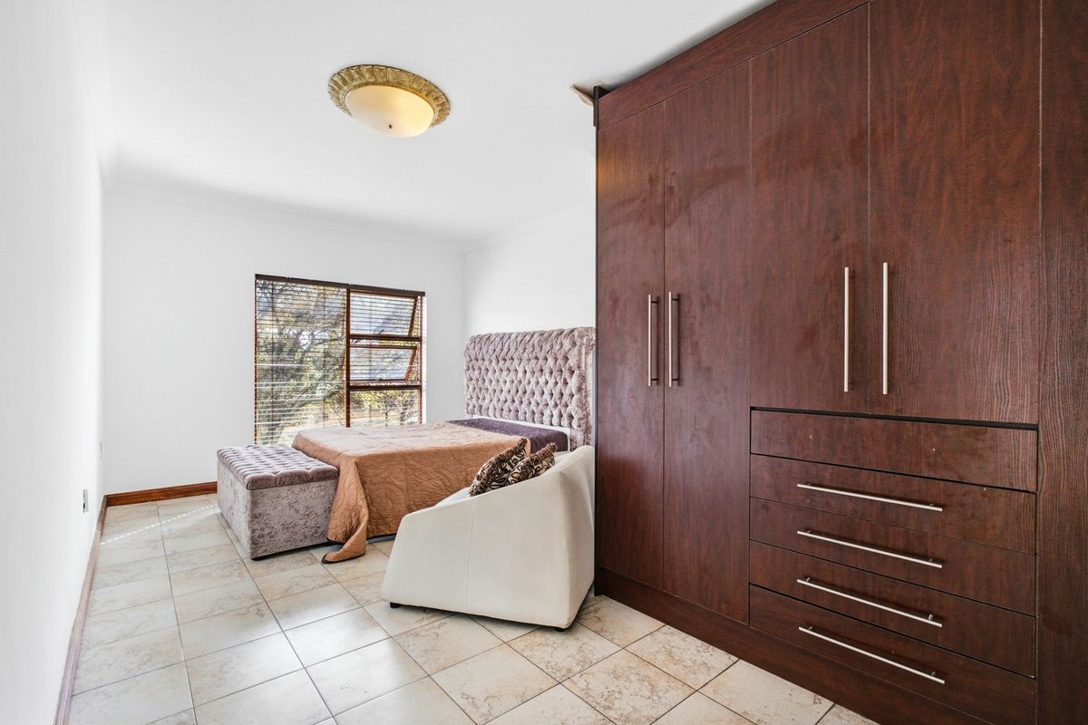 Spacious bedroom featuring large built-in wooden cupboards, tiled flooring, and natural light through a large window.