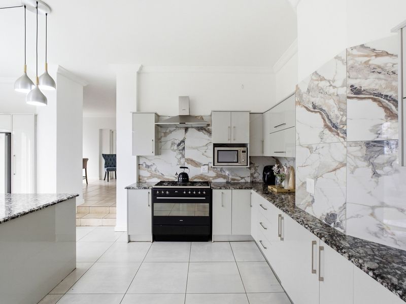 Modern kitchen featuring granite countertops, marble-look splashback tiles, built-in oven with gas hob, extractor fan, and sleek cabinetry.