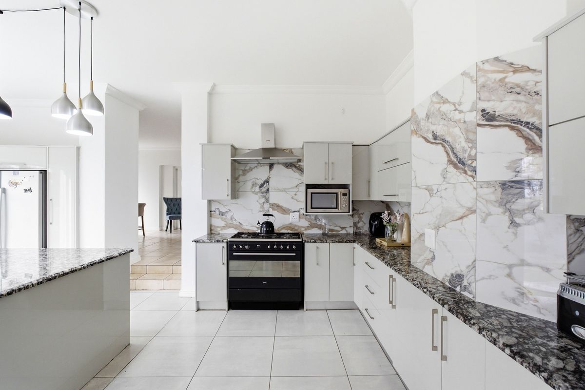 Modern kitchen featuring granite countertops, marble-look splashback tiles, built-in oven with gas hob, extractor fan, and sleek cabinetry.