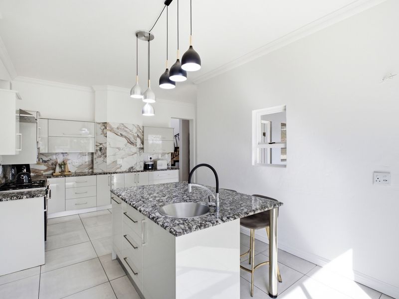 Modern kitchen featuring high-gloss cabinetry, granite countertops, a central island with a prep sink, and stylish pendant lighting.