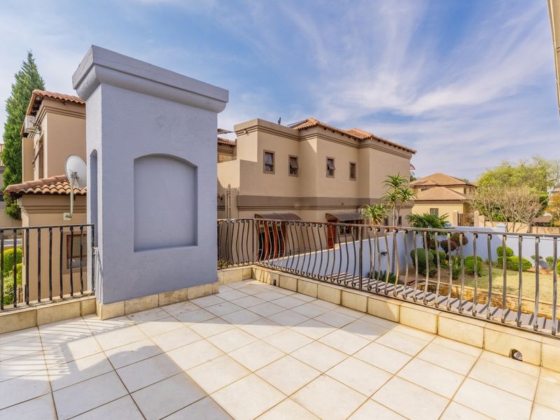 A spacious upper-level balcony featuring tiled flooring and a decorative wrought iron balustrade, overlooking the surrounding residential estate.