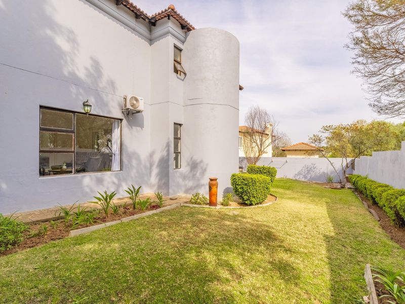Rear view of the property featuring a well-maintained garden, perimeter wall, and exterior wall-mounted air conditioning unit.