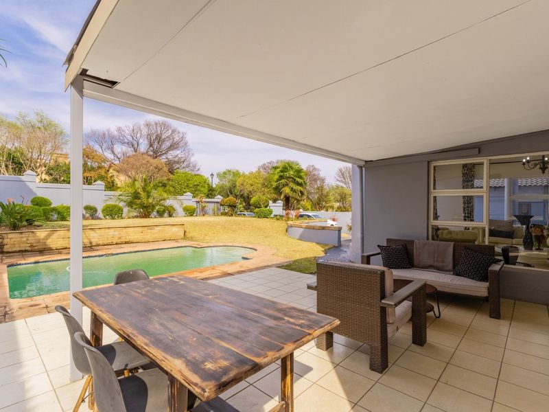 A covered patio area featuring tiled flooring, overlooking a private swimming pool and landscaped garden, ideal for outdoor entertaining.
