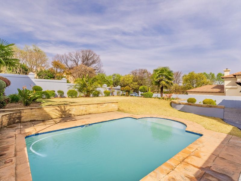A well-maintained outdoor pool area featuring a paved surround, retaining walls, and a landscaped garden with boundary walls.