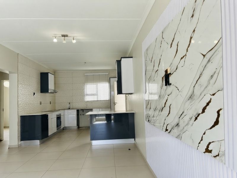 Modern open-plan kitchen and living area featuring sleek two-tone cabinetry, stone countertops, integrated appliances, and a decorative marble-effect feature wall.