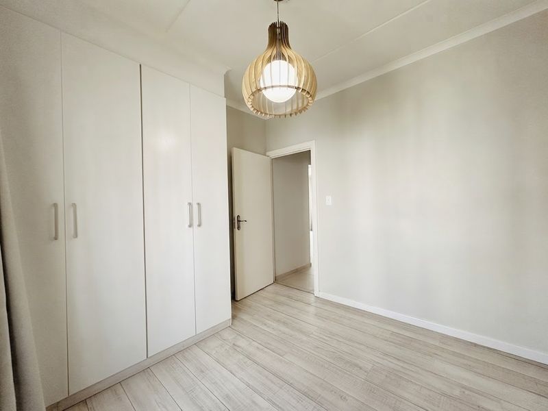 A bright, empty bedroom featuring light-toned laminate flooring and ample built-in cupboard storage, offering a clean and neutral space ready for personalization.