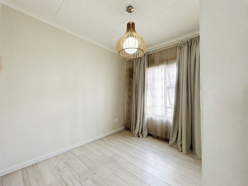 A bright, empty bedroom featuring light-toned laminate flooring, neutral walls, and a modern pendant light fixture.